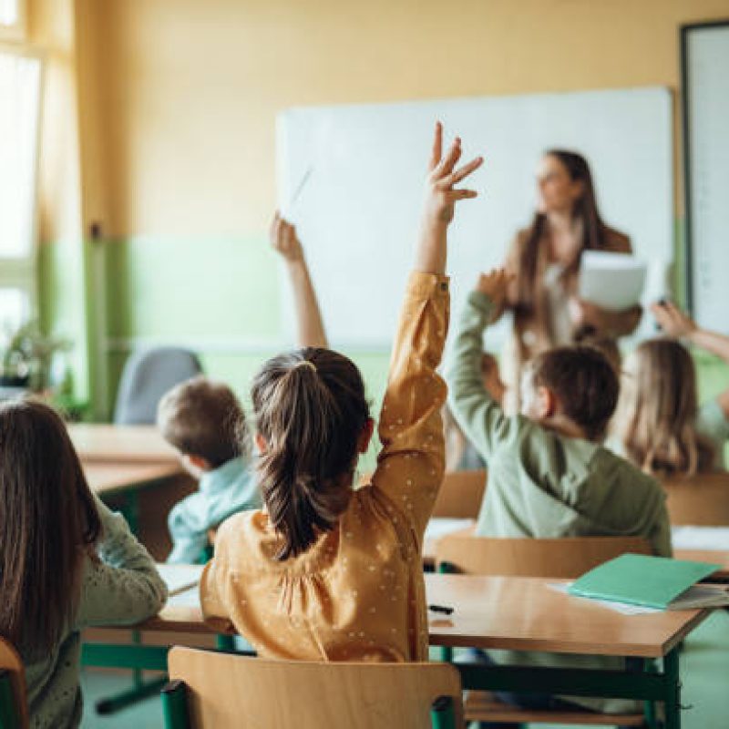 Students raising hands while teacher asking them questions in classroom