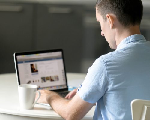 Portrait of a young man working at the desk with a laptop, looking at the screen, education, business concept photo. View over the shoulder, rear view